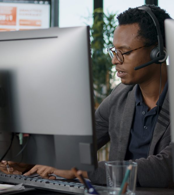 African american employee using headset at customer service job, asnwering call about telemarketing sales. Male operator working at call center office to help clients on helpline.